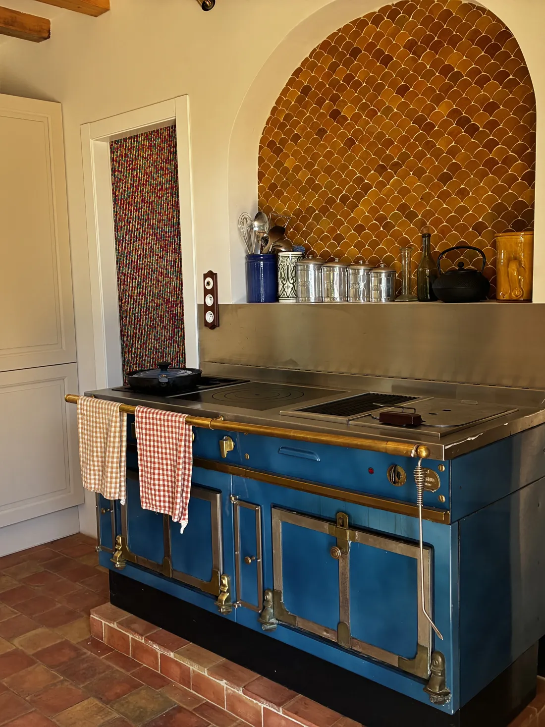 Piano de cuisson bleu sous une niche cintrée en tomettes écailles, cuisine d'un mas rénové